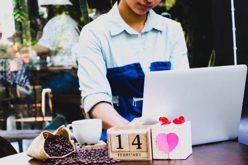 Business women using laptop and drinking coffee with 14 February wooden calendar in Valentine day