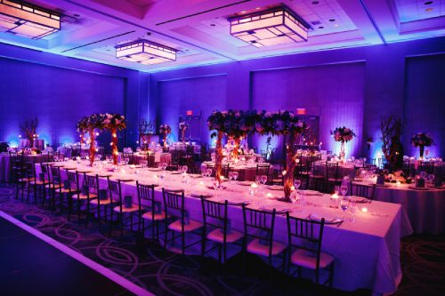 Decorated banquet hall with flowers, rectangle table, chiavari chairs, candles in violet colours